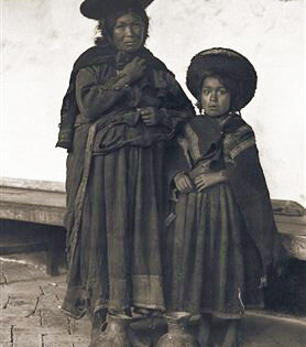 Foto: Hiram Bingham. Muchachas andinas. Una de ellas sostiene una vara de medir para ofrecer cierta idea de su estatura. Visten el atuendo propio de las indias montañesas peruanas. El tocado es un sombrero plano de paja forrado de franela roja por un lado y de panilla azul con cinta trenzada dorada por el contrario. Se lleva de uno u otro lado en función del tiempo que haga. Los bordes del sombrero hacia arriba indican que hace buen tiempo.